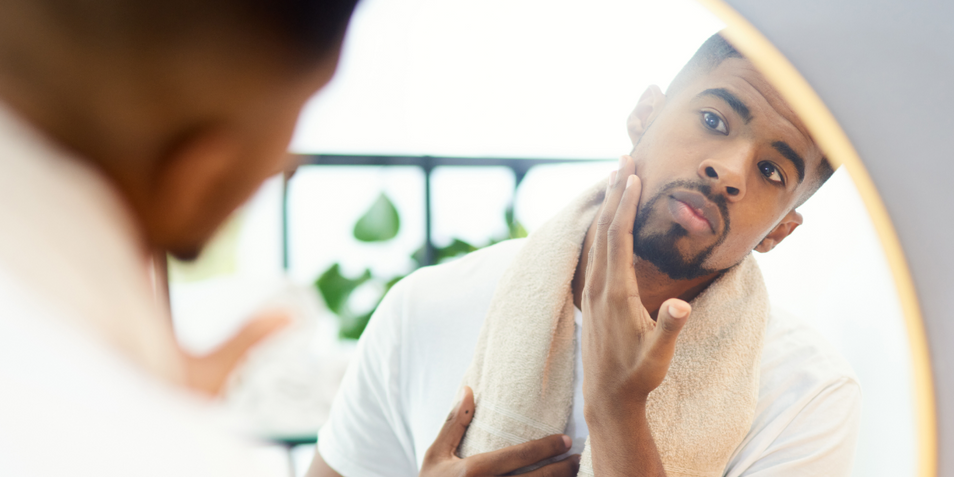 A man touching his face with a healthy glow in front of a mirror