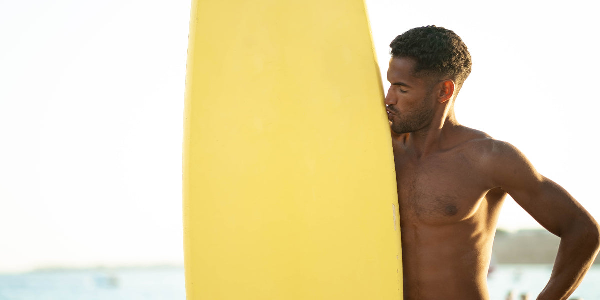 A bearded man holding a surfboard.
